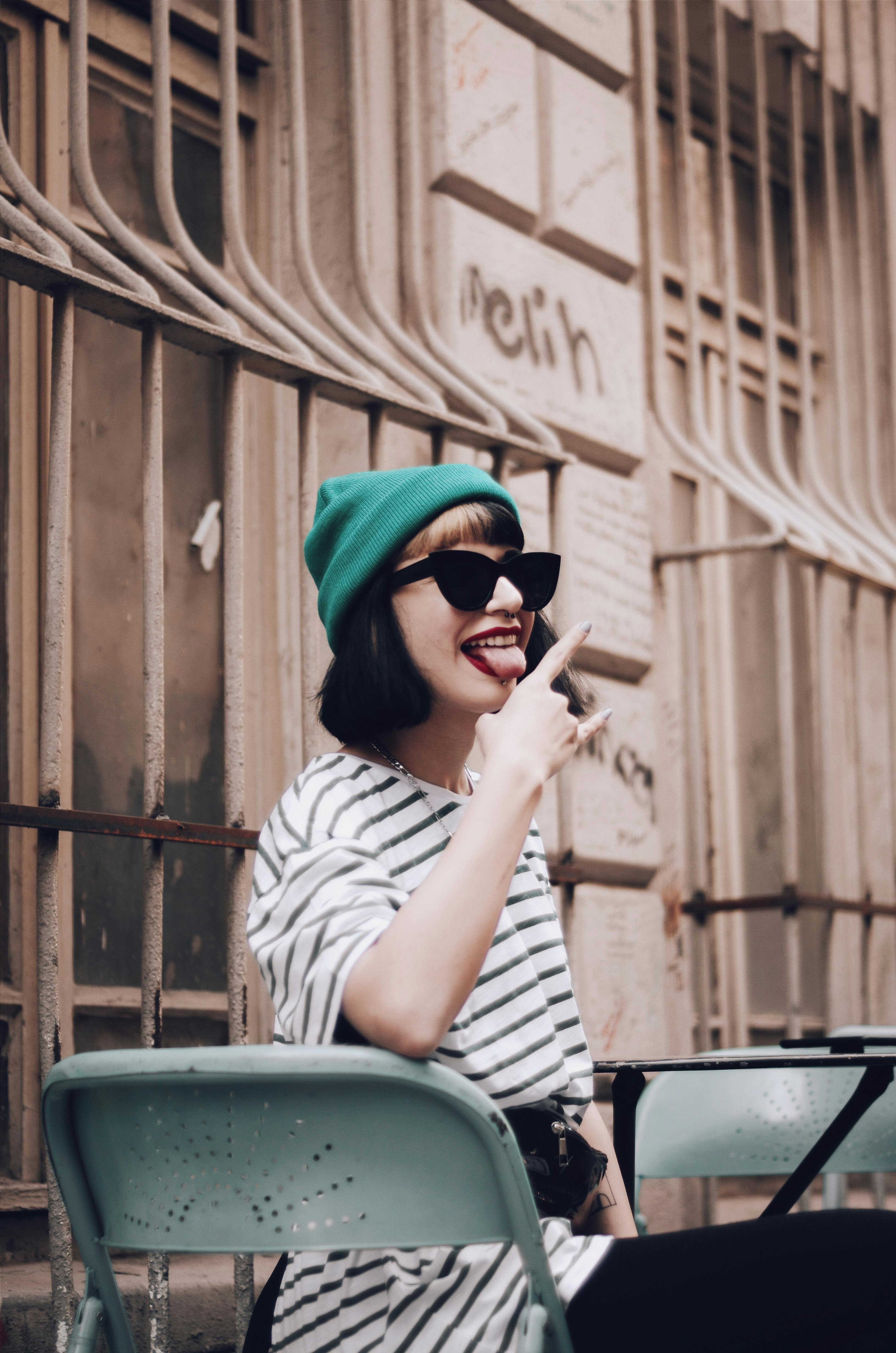Stylish woman in sunglasses and green beanie posing outdoors in a casual striped top.