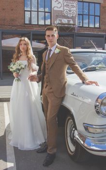 Bride and groom posing elegantly beside vintage car, celebrating their wedding day outdoors in style.