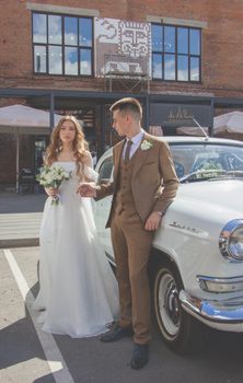 A bride and groom pose beside a classic car in an outdoor ceremony setting, exuding romance and elegance.