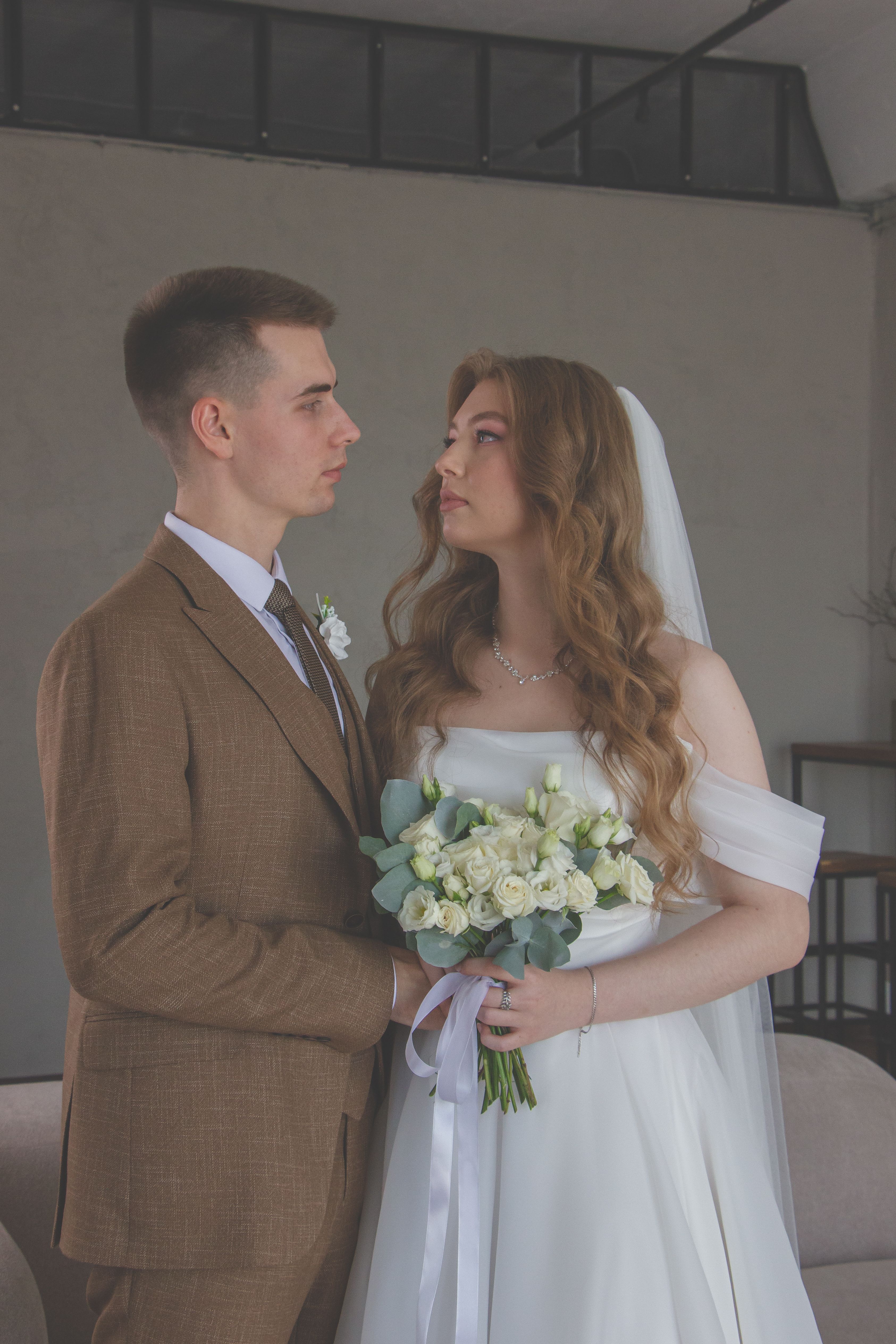 A bride and groom standing in front of a white wall · Free Stock Photo