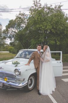 Bride and groom pose elegantly by a vintage car on a beautiful day.