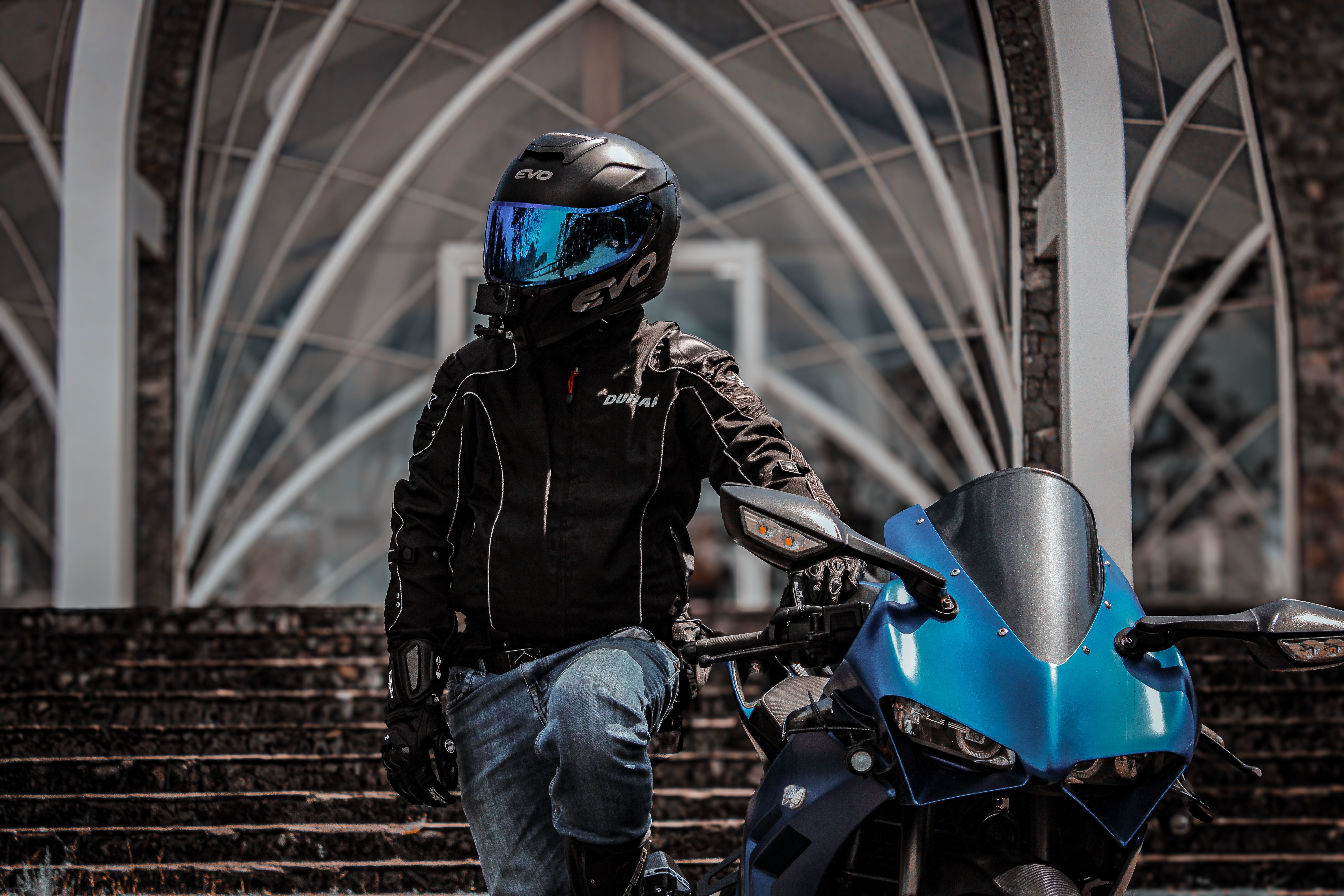 Motorcycle rider in helmet stands with sports bike in urban setting.