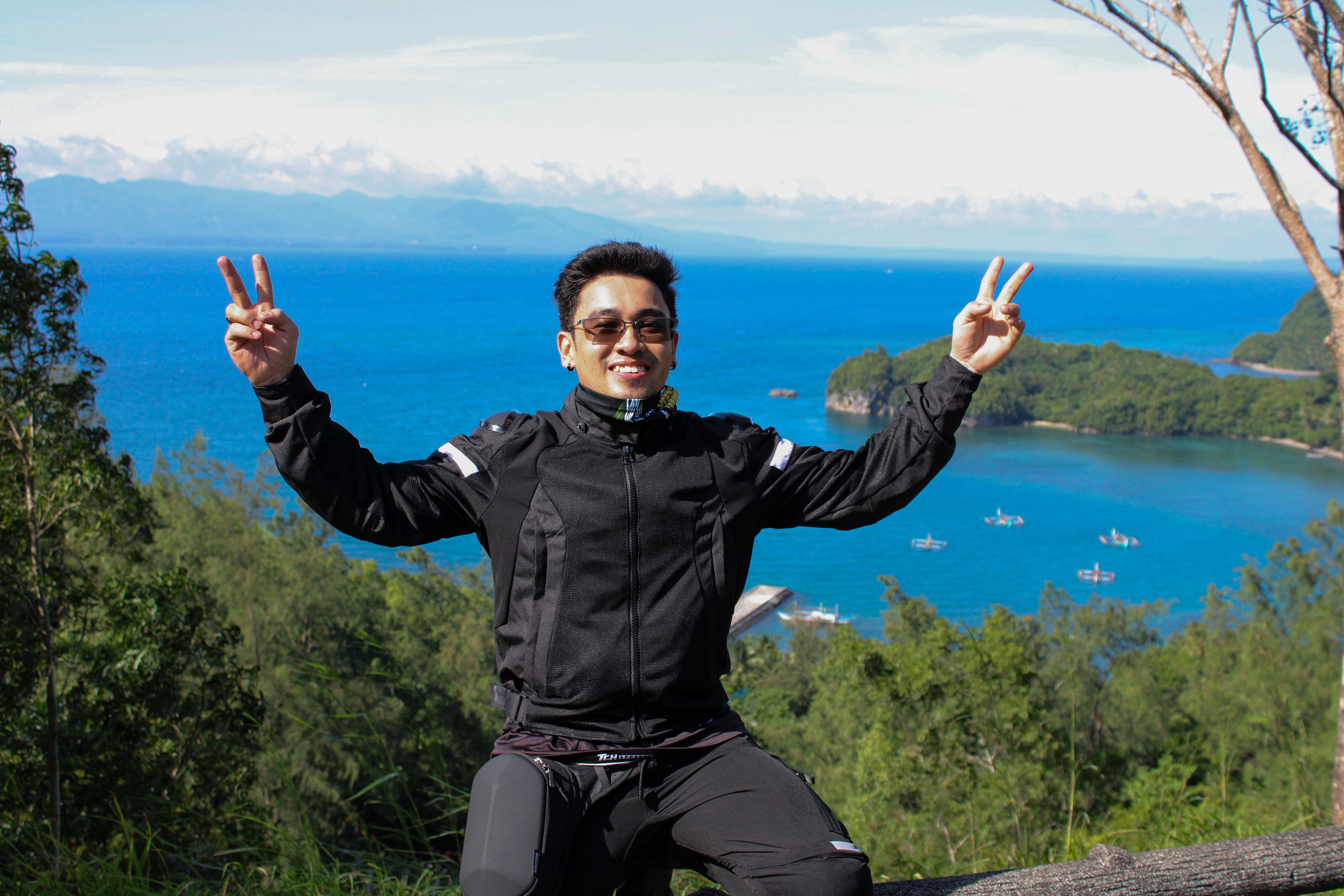 Man enjoying a scenic ocean view with victory signs and a sunny summer backdrop.