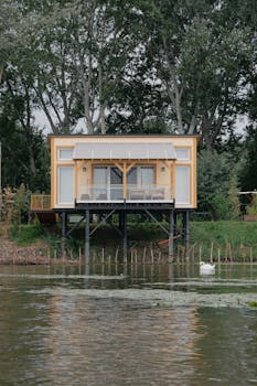 A modern wooden house on stilts by a peaceful river, surrounded by lush greenery in Hungary.