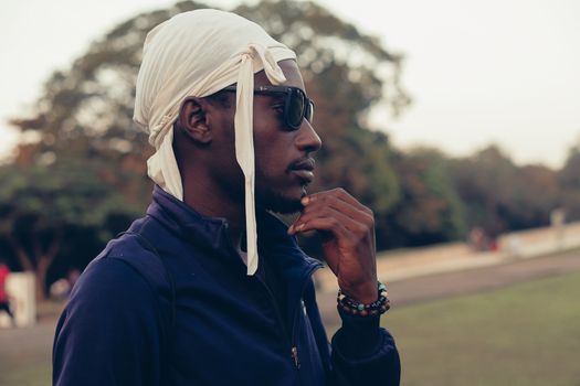 Stylish man wearing sunglasses in a park during the daytime, showcasing a thoughtful pose.