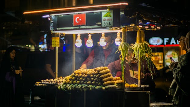 Vibrant outdoor Turkish street market stall featuring grilled corn cobs, bustling with people at night.
