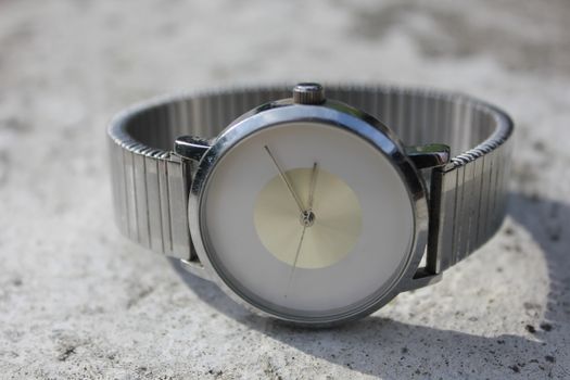 Close-up of a minimalist silver wristwatch on a concrete surface. Timeless elegance.