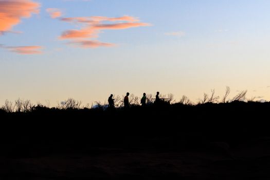 A group of people walking along a ridge at sunset, silhouetted against a serene sky.