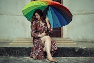 一位穿着花卉连衣裙的时尚女性坐在户外的彩虹伞下