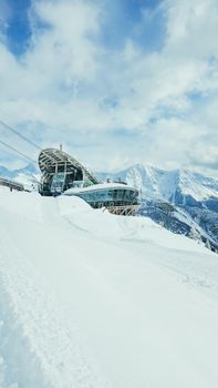 A modern architectural ski resort nestled in snowy Alpine mountains under a bright blue sky.