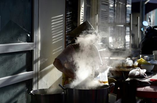 A person wearing conical hat cooking with steam rising in an outdoor setting.