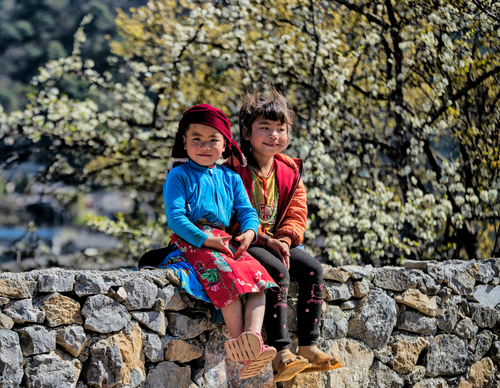 Free Two children sitting on a stone wall, enjoying a sunny spring day in Hà Giang, Vietnam. Stock Photo