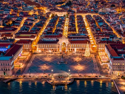 Free Stunning aerial view of Lisbon's Praça do Comércio at dusk with vibrant city lights and illuminated streets. Stock Photo