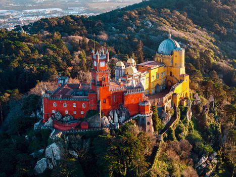 Breathtaking aerial shot of the colorful Pena Palace nestled in the lush hills of Sintra, Portugal.