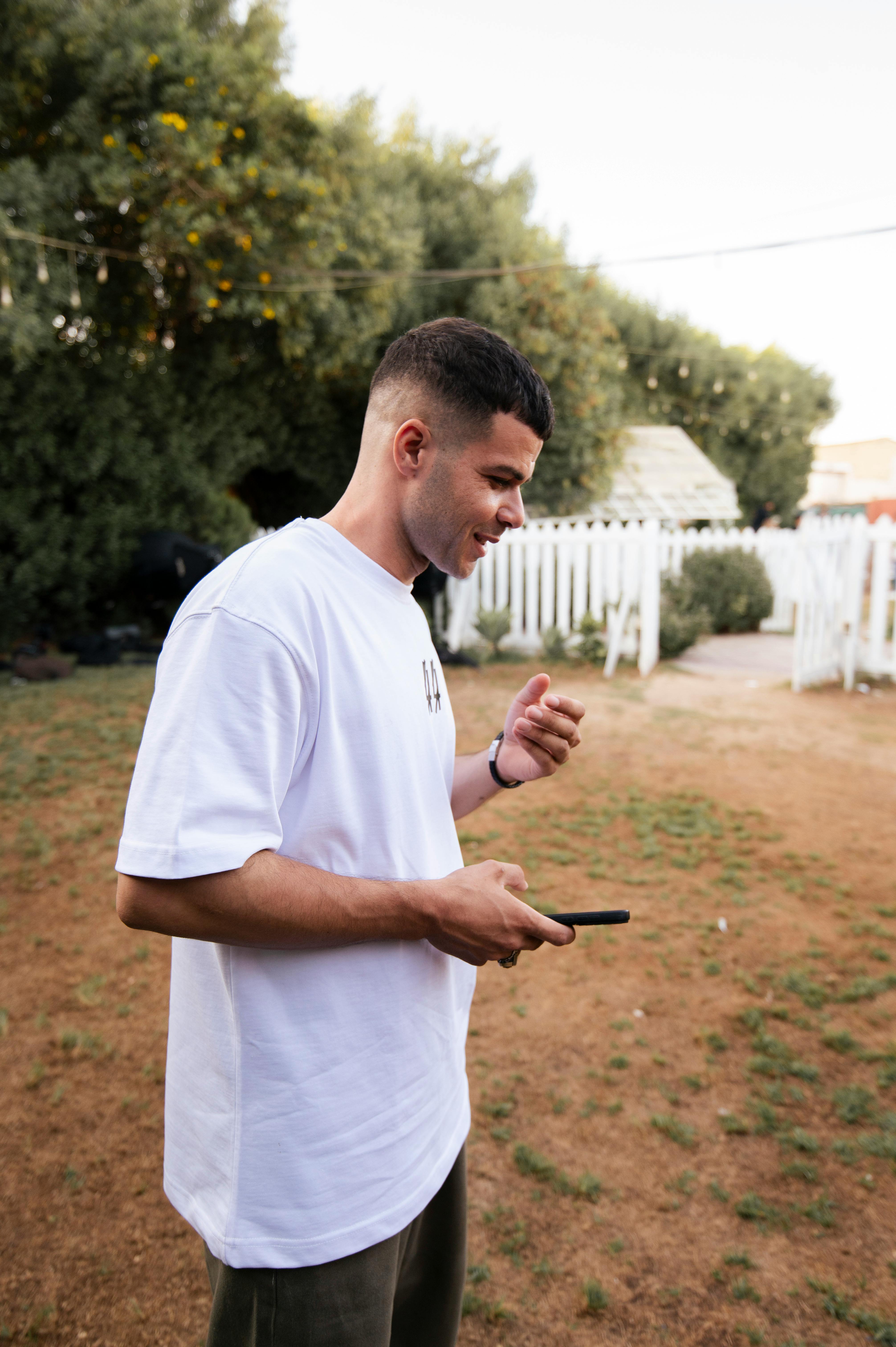 a man in a white shirt and black pants is looking at his phone