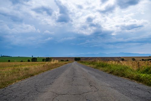 Free A tranquil rural road in Žilina, Slovakia stretches through lush countryside under a dramatic sky. Stock Photo