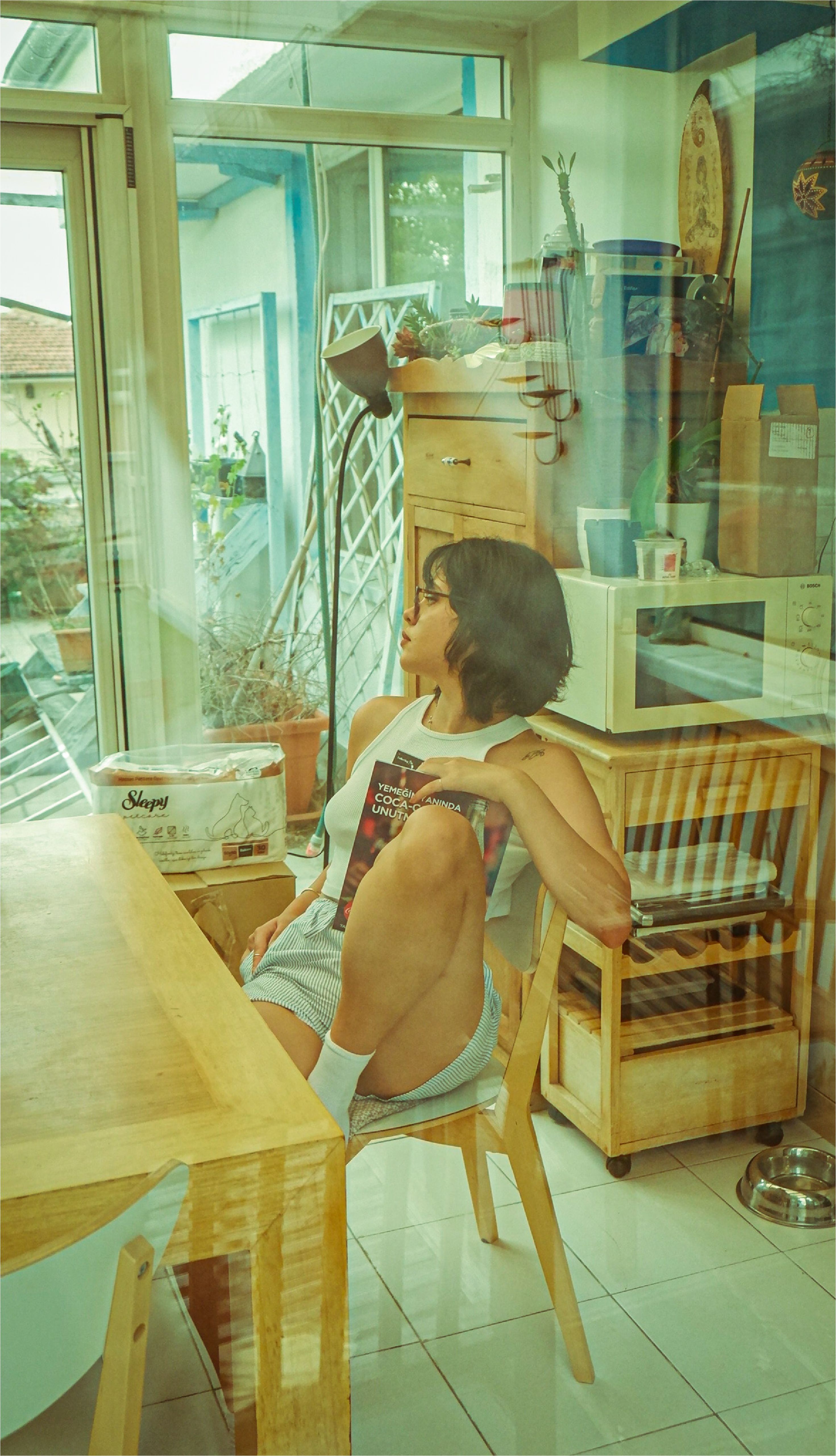 Woman sitting in a cozy room, surrounded by indoor plants and furniture, reflecting peacefully.