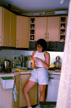 A young woman in casual attire preparing food on a modern kitchen countertop.