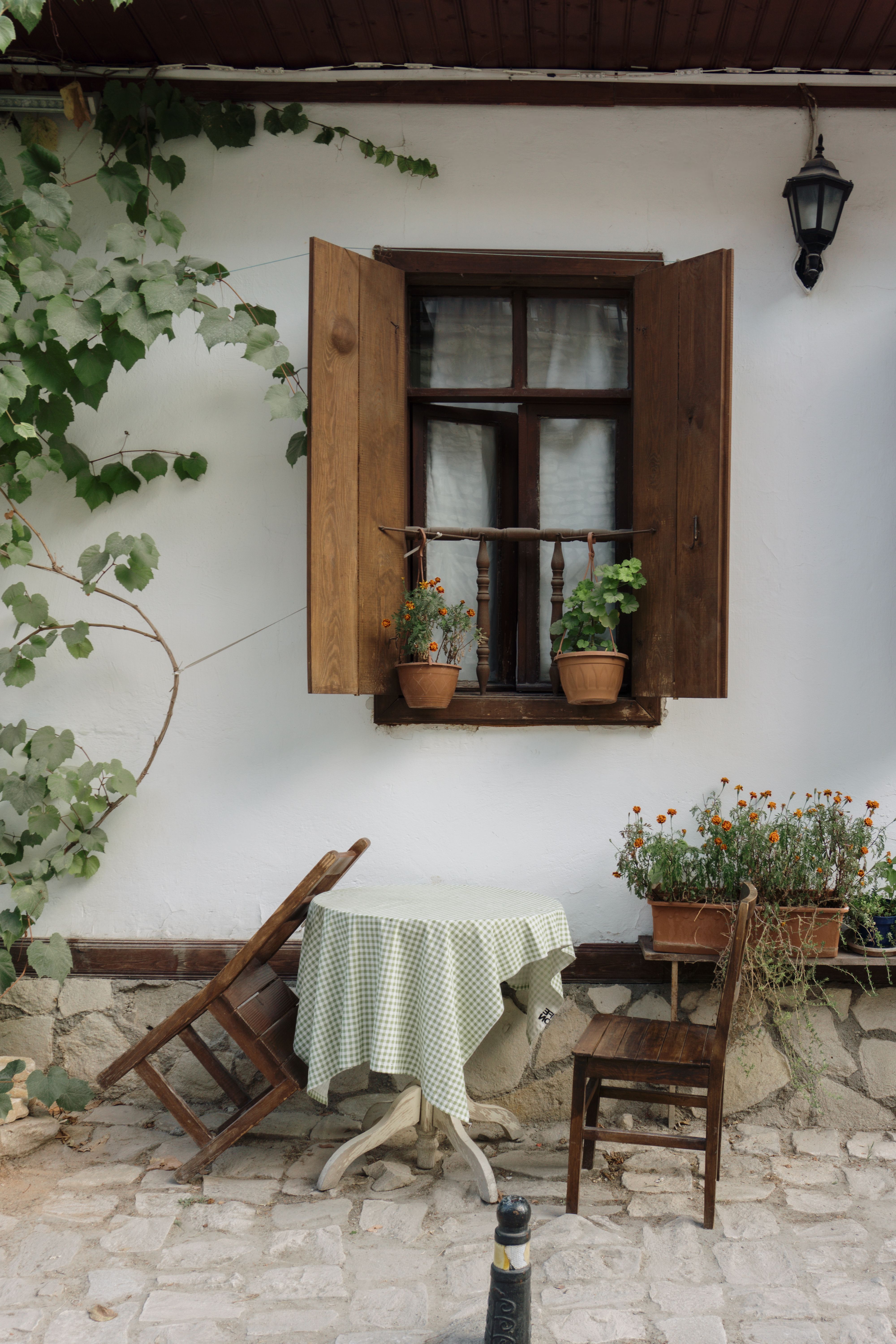 A cozy patio scene featuring a wooden window, chairs, and lush greenery, perfect for relaxation.