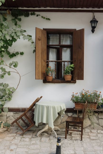 A cozy patio scene featuring a wooden window, chairs, and lush greenery, perfect for relaxation.