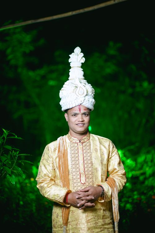 Free A groom in traditional South Asian attire posing outdoors with a vibrant green backdrop. Stock Photo