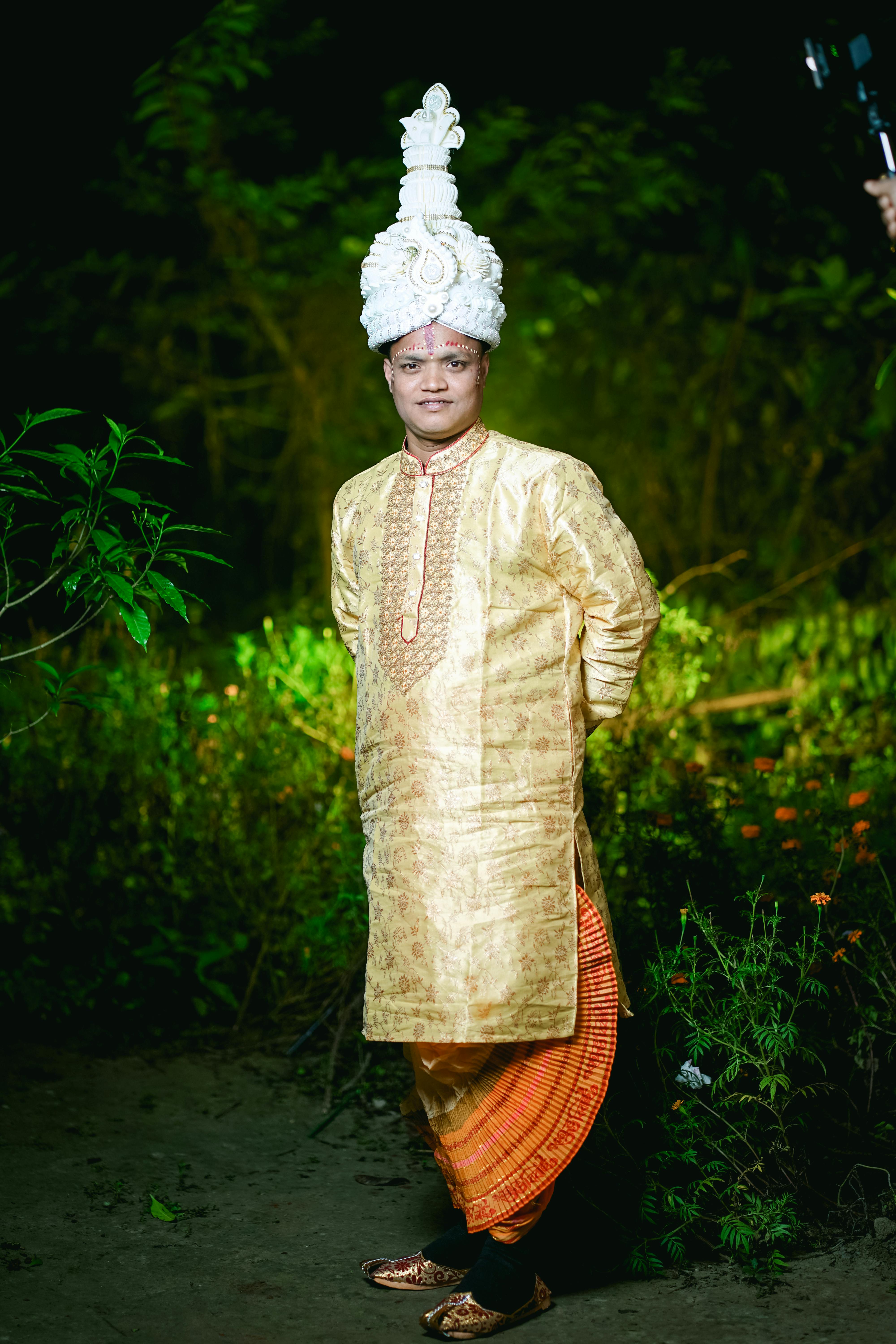 A Bengali groom in traditional wedding attire poses outdoors at night.