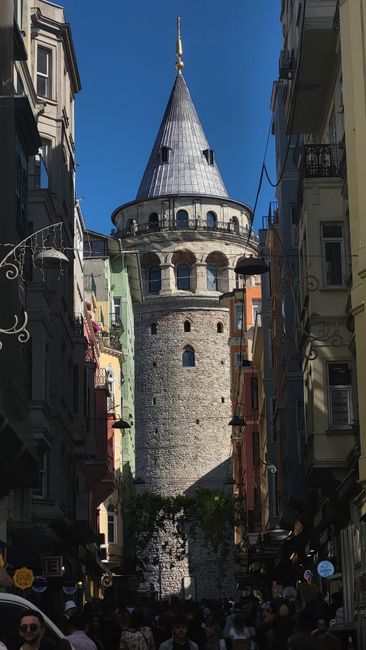 Historic Galata Tower surrounded by colorful buildings in Istanbul, bustling street view.
