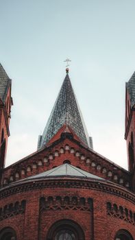 Close-up of a red brick Gothic cathedral with dramatic spires and a cross.