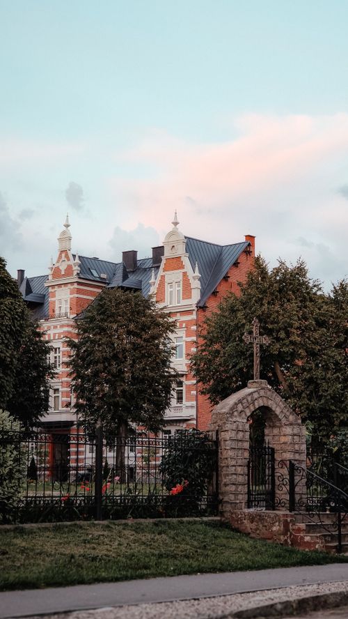Free Charming historical building with intricate architecture, surrounded by lush gardens and trees in soft daylight. Stock Photo