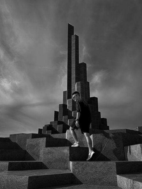 Black and white photo of a man on modern architectural monument with dramatic clouds.