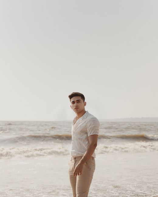 A young man standing on a tranquil beach under the bright summer sky, enjoying the scenery.