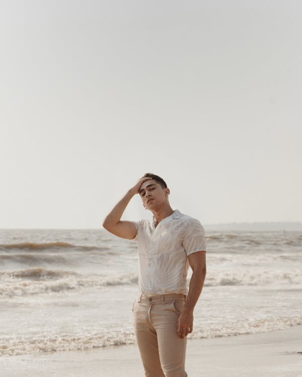 Hombre Vestido Con Camisa Blanca Y Pantalones Beige De Pie Cerca De La Orilla Mar · Foto de stock gratuita