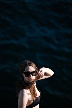 Elegant woman in sunglasses relaxes by the ocean during sunset, showcasing fashion and leisure by the sea.