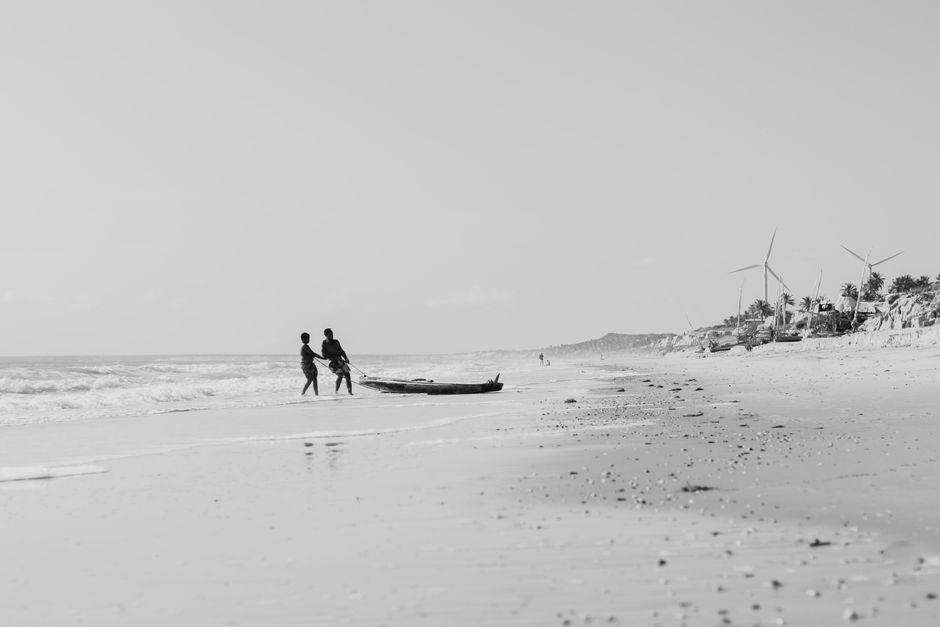 A serene black and white image of fishermen on a Brazilian beach with wind turbines in the background.