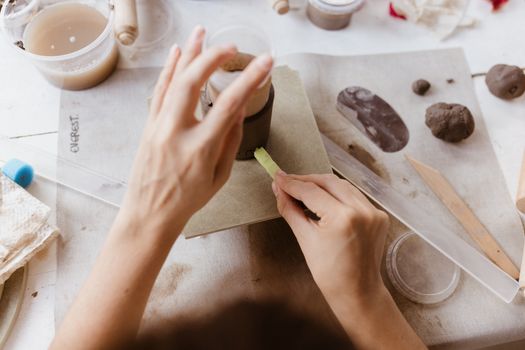 Close-up of hands working with clay and tools, crafting pottery indoors.
