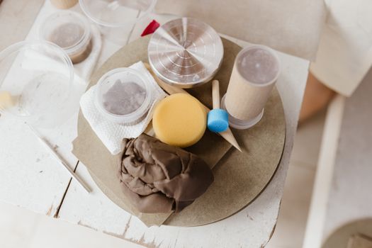 Artistic arrangement of ceramic crafting tools including clay, sponges, and brushes on a rustic table.