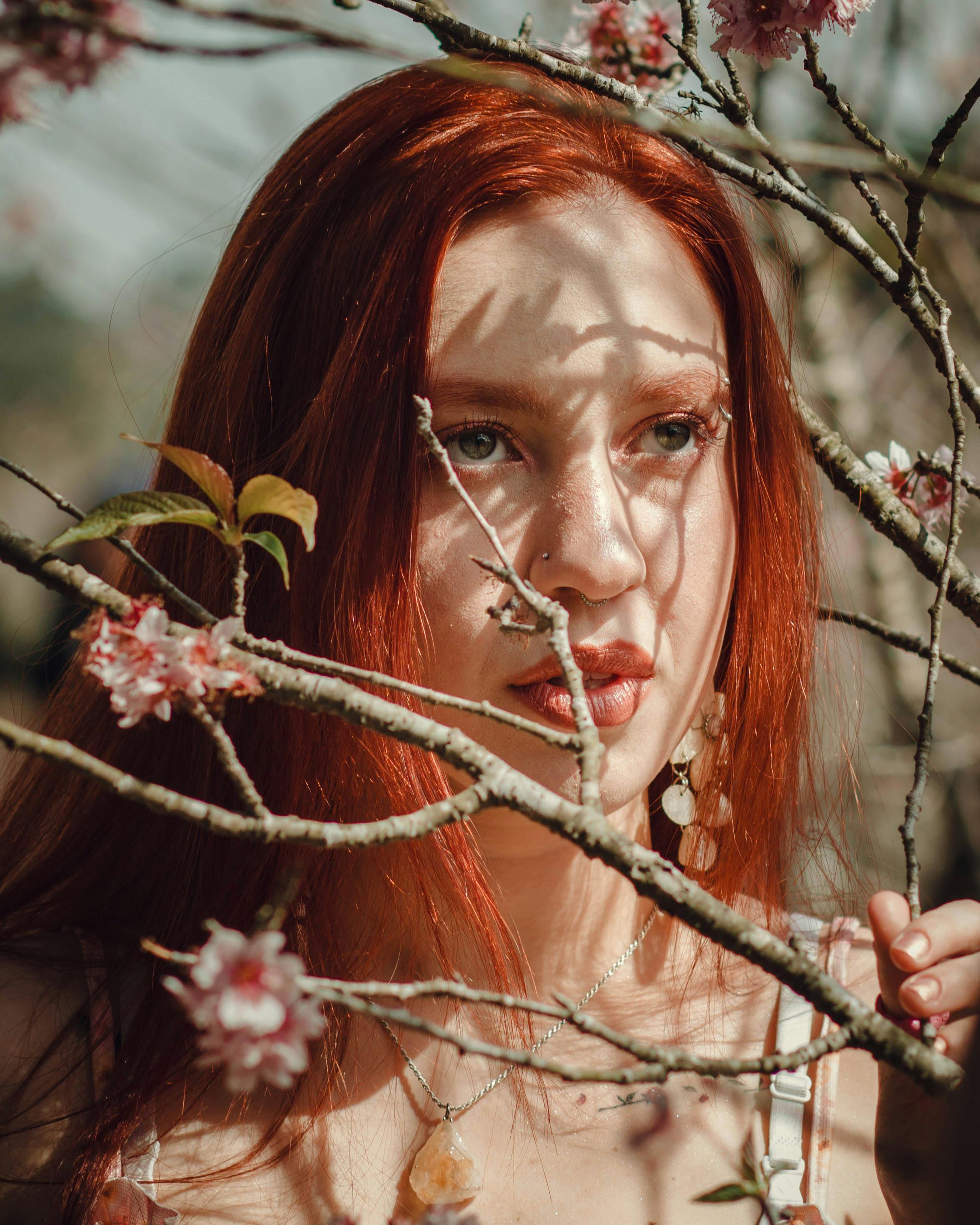 a young redhead standing behind the branches in sunlight