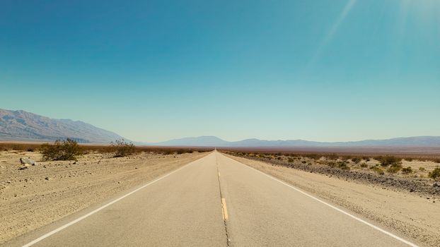 Long straight highway through a desolate desert under a clear blue sky.