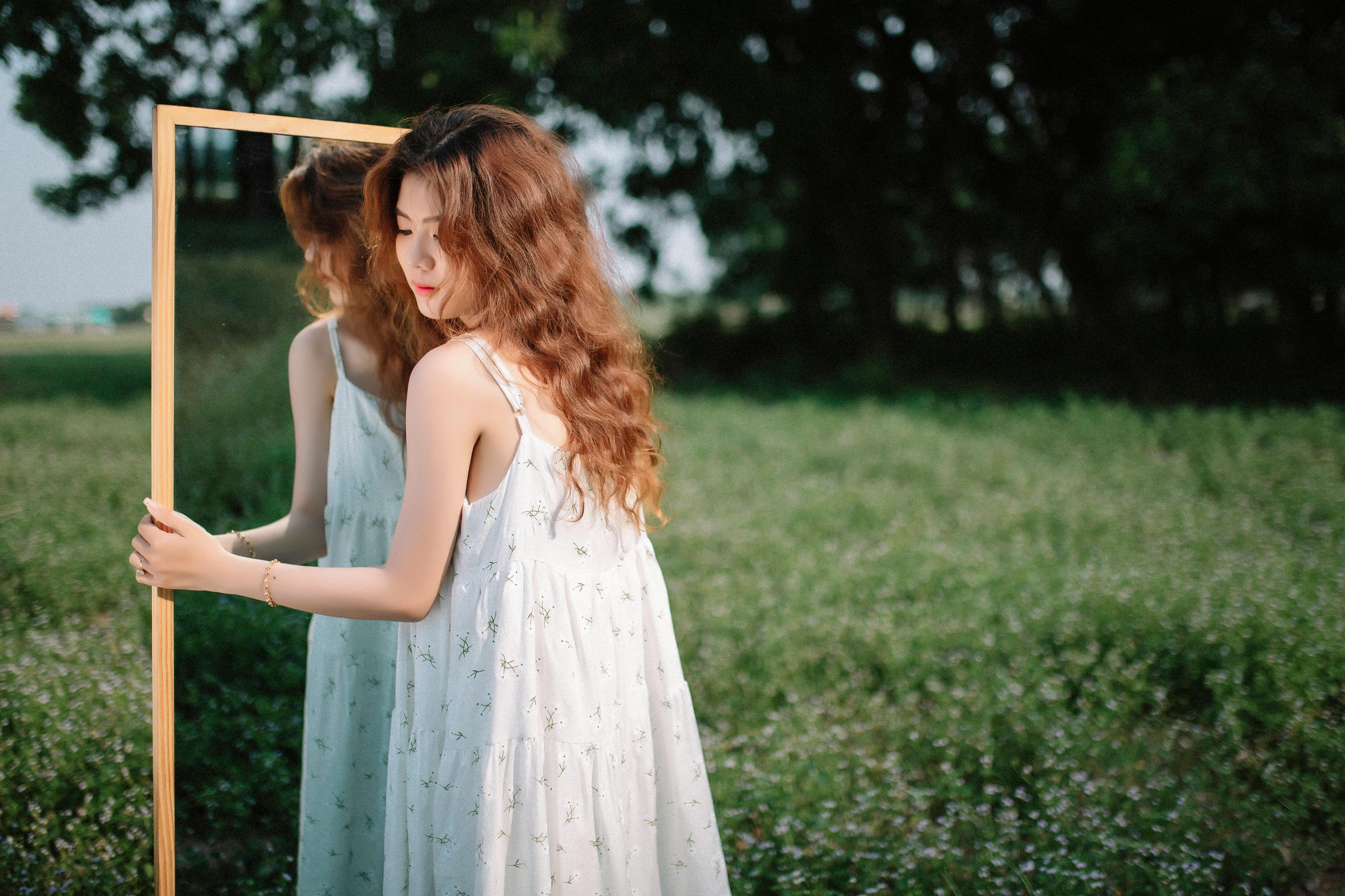 a woman in a white dress is looking at a mirror