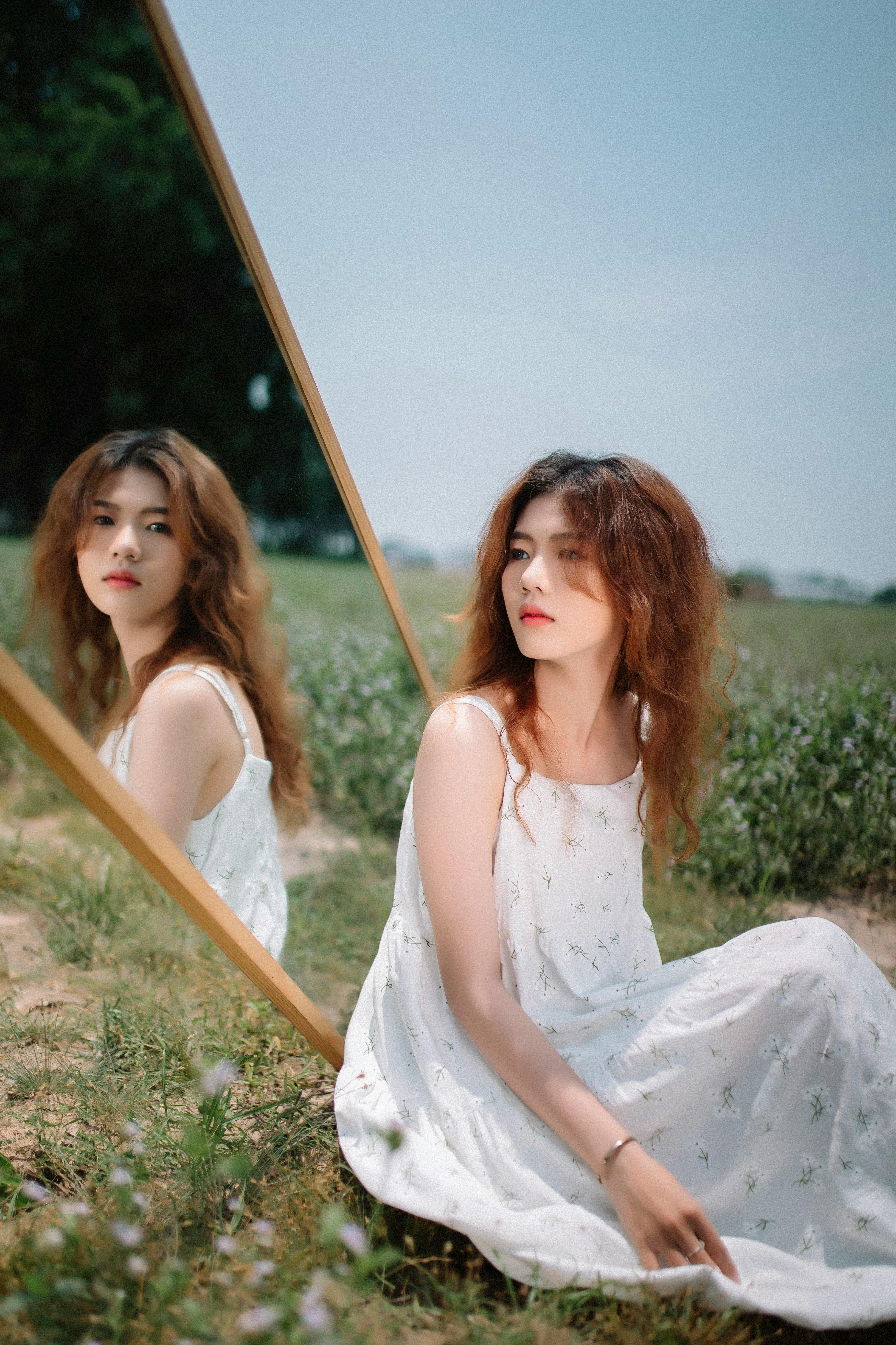 A woman in a white dress reflecting in a mirror outdoors on a sunny day.