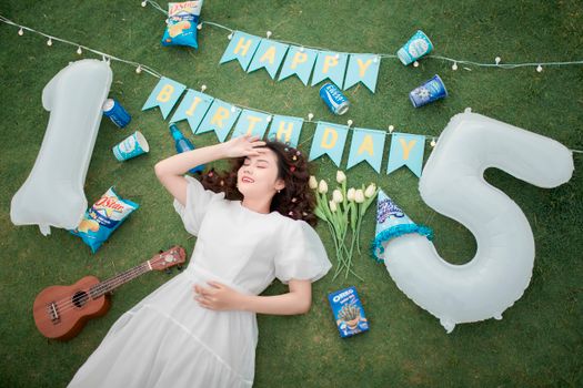A young woman in white dress celebrating her birthday outdoors with decorations and snacks.