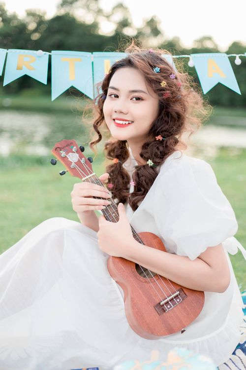 Free A young woman joyfully playing ukulele in a park setting with festive decorations. Stock Photo