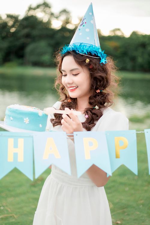 Free Young woman celebrates birthday outdoors with cake and party hat by a lake. Stock Photo