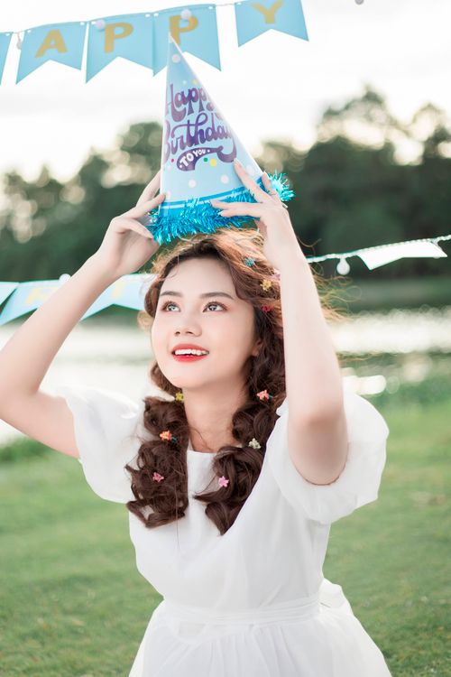 Free Teen girl in white dress celebrating birthday outdoors with a party hat. Stock Photo