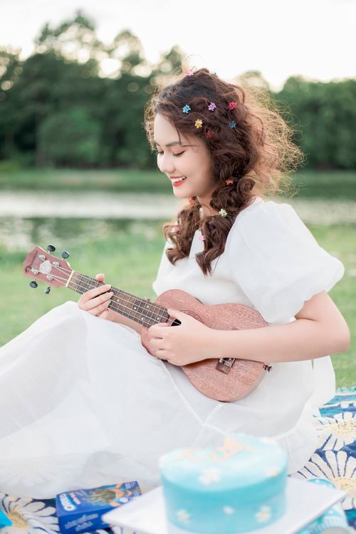 Free A young woman plays the ukulele in a serene outdoor setting, surrounded by nature. Stock Photo