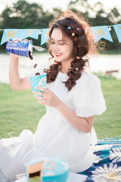 Free Young woman wearing floral dress enjoying a sunny day picnic by the lake. Stock Photo