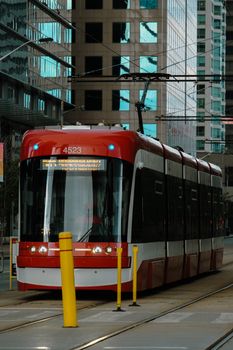 A red streetcar navigates through downtown Toronto's urban landscape, showcasing city transport.