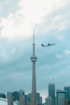 Skyline view of Toronto's CN Tower with a passing airplane against a cloudy sky.