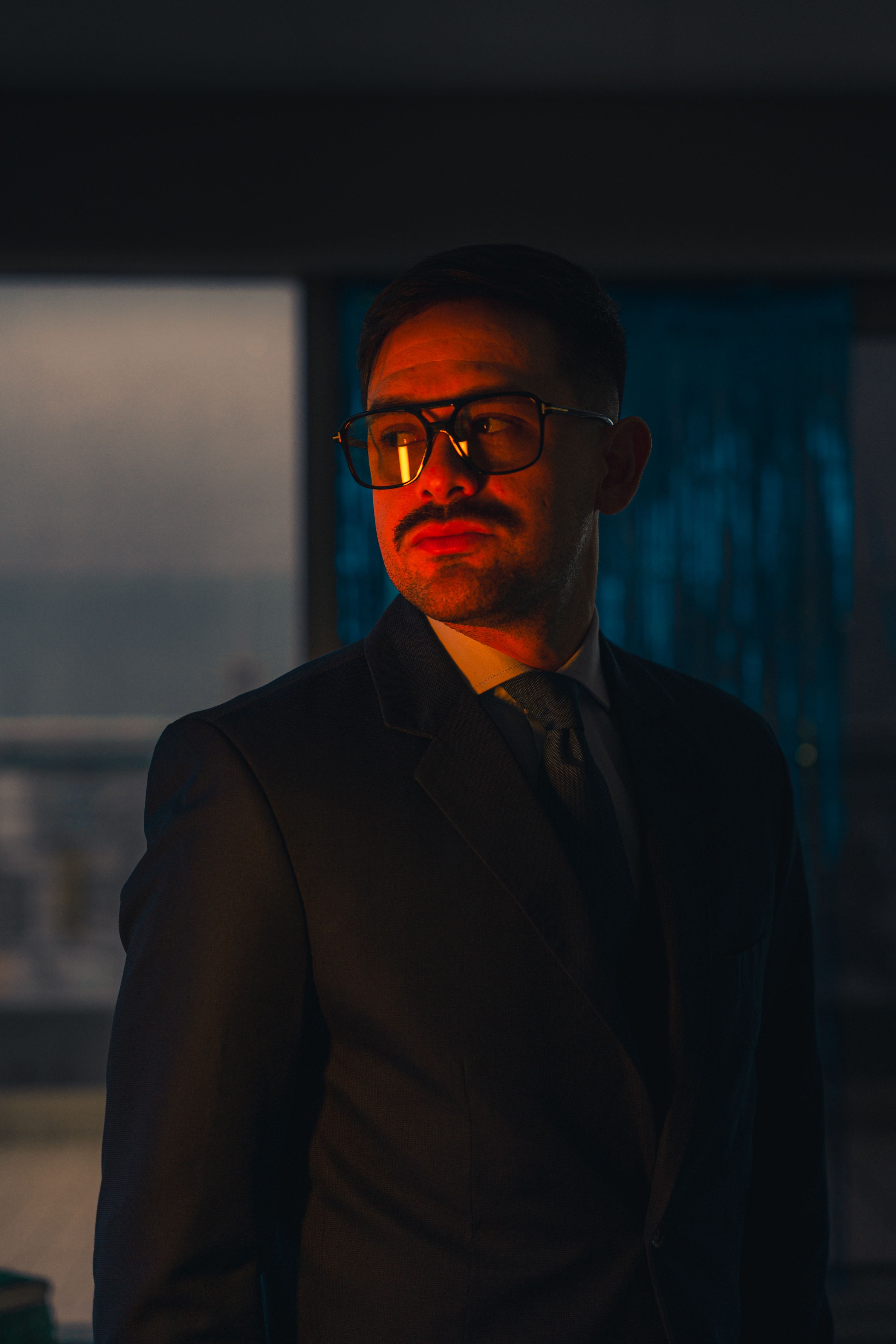 Confident man in a suit and sunglasses, dramatic lighting indoors.