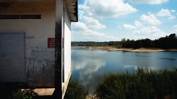 A serene lake view with a rustic building, lush greenery, and clear skies.
